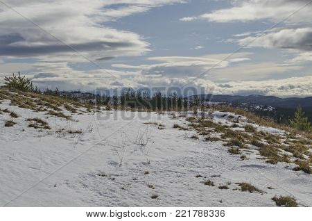 Majestic view of cloudy sky, winter mountain, snowy glade, residential district, conifer and deciduous forest from Plana mountain toward Rila mountain, Bulgaria, Europe