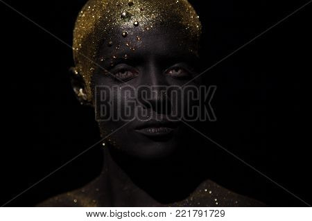 Portrait of a beautiful woman with creative body art glowing make up. Face is colored with black paint.