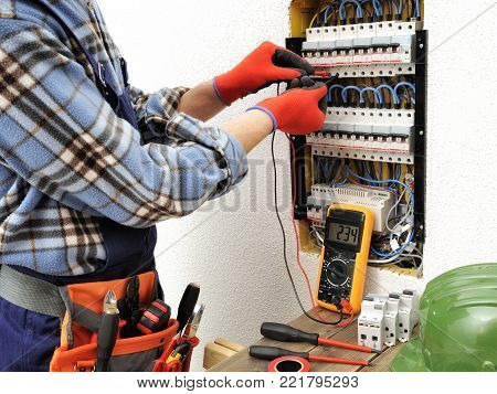 Young electrician technician measures with a multimeter the voltage in a electrical panel