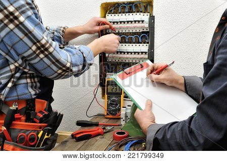 The engineer writes on a notepad the measurement of the voltage of the electrical panel detected by the young electrician