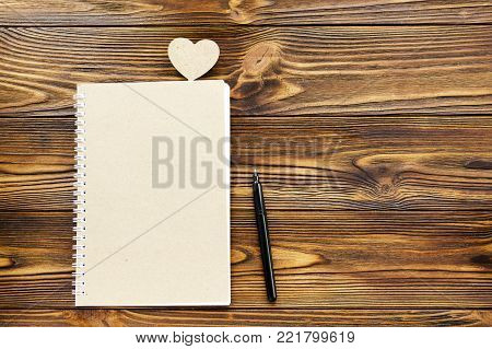 kraft paper notepad, pen. wooden heart on wooden background and copy space