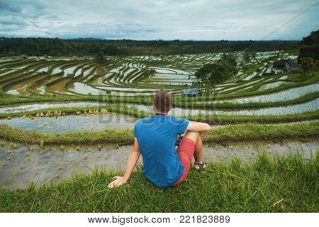 Young Man Traveler sitting and relaxing outdoor at rice fields on terraced in Bali Indonesia. Concept of rural travelling in Asia