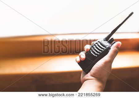Man's hand holding portable walkie-talkie in office.