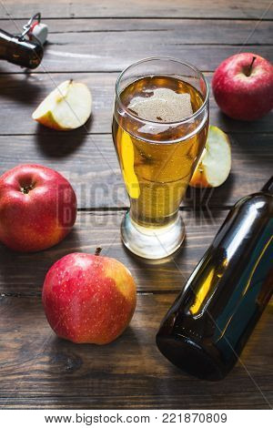 Glass of cider with apples and bottle on rustic wooden background.