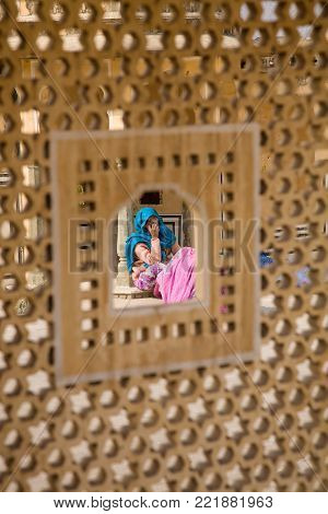 Jaipur, India - 2014, December 31 : A woman in traditional Rajasthani dress seen through an opening in a jali which is a typical latticed stone screen used in India