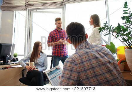 Group of young modern people in smart casual wear having a brainstorm meeting while standing in the creative office