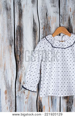 Girls' top on wooden hanger. Ruffle collar and cuffs, white blouse decorated with nautical pattern. Sleepwear for kids.