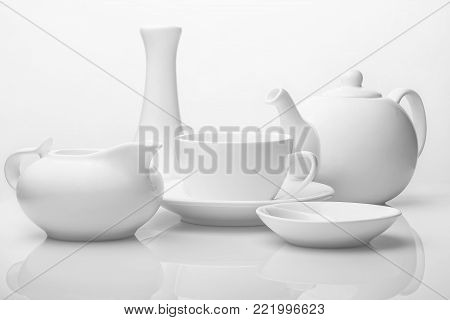 The tea set is white on a white background. Teapot, creamer, Cup, saucer, and vase on the table. Ceramic kitchenware. Studio light.