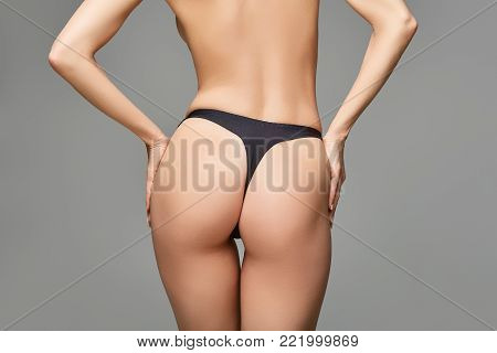 beautiful young woman fit butt on in black panties. studio shot on grey background. copy space.