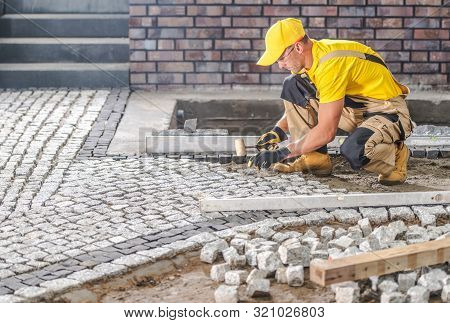 Professional Caucasian Worker Building Granite Paved Hardstanding Garden Path. Industrial Theme.