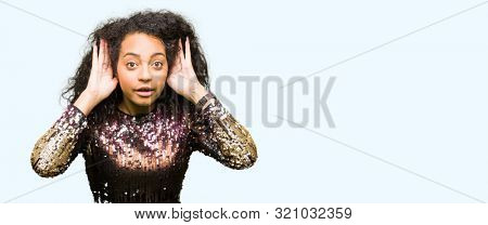 Young beautiful girl with curly hair wearing night party dress Trying to hear both hands on ear gesture, curious for gossip. Hearing problem, deaf