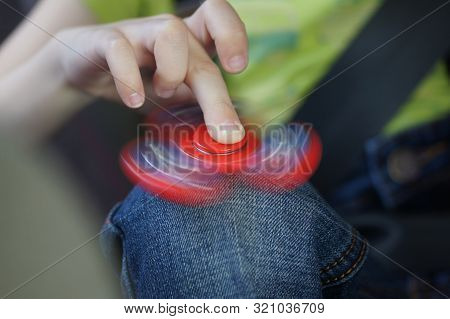 Child's Hand Holds A Spiner Spinning On His Knee. Pastime In The Car. Games On A Long Trip In The Ca