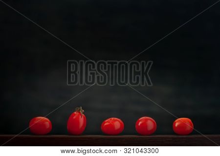 Small Red Tomatoes Lie In A Row, One Stands Out And Stands. Side View. Shelf Store Or Market. Can Be