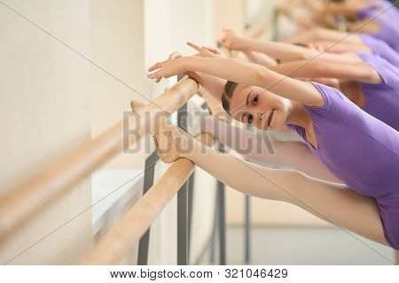 Ballet Girls Stretching On Ballet Barre. Young Ballerina Training Her Flexibility At Ballet Dance Le