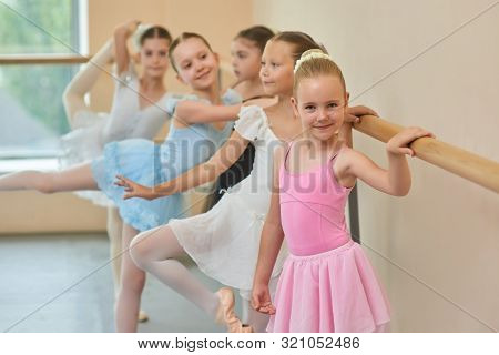 Happy Smiling Ballerina In Pink Suit. Adorable Little Ballet Girl Standing At Ballet Barre In Studio