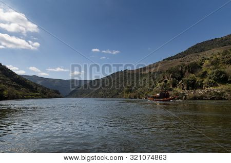 Scenic View Of The Douro River With A Traditional Rabelo Boat And Terraced Vineyards Near The Tua Vi
