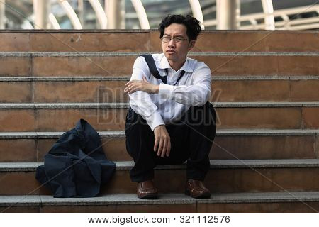 Depressed Stressed Young Asian Business Man In Suit With Hands On Head Sitting On Stairs. Unemployme