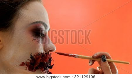 Bodypainting. A Hand With A Brush Puts Bloody Paint On The Sewn Mouth Of Another Girl. The Process O