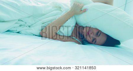 Young caucasian woman covering her head and ears with pillows