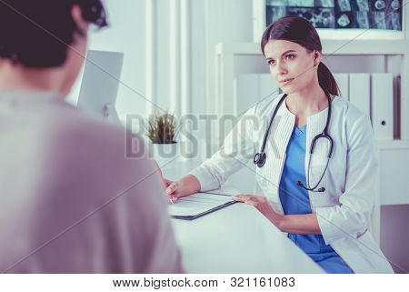 Doctor and patient discussing medical problems in a hospital consulting room. Doc filling in a patient's form