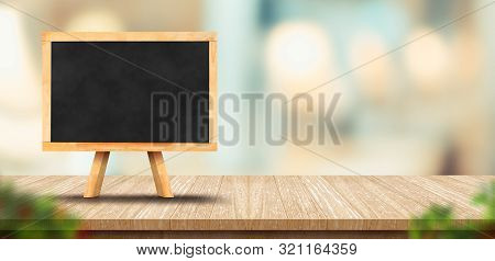 Wood Table With Blank Blackborard Menu And Blurred Leaf Foreground Leaf In Restaurant With Bokeh Bac