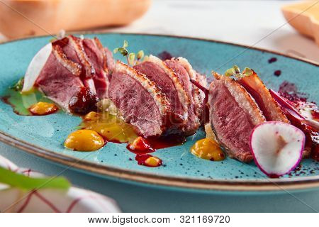 Macro shot of Sliced duck breast with hummus and plum sauce on turquoise plate. Exquisite serving restaurant main course with grilled goose fillet steak, greens and spices