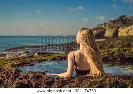 Young Woman Tourist On Pantai Tegal Wangi Beach Sitting In A Bath Of Sea Water, Bali Island, Indones