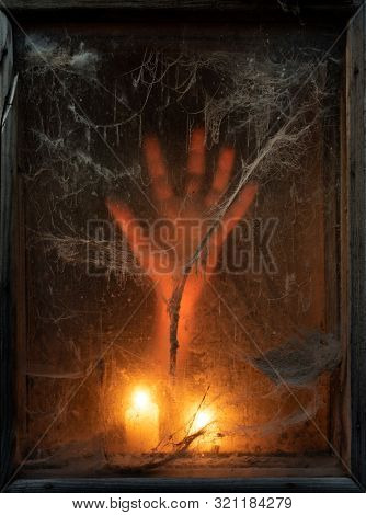Scary halloween background with creepy old spider web (cobwebs) in a dark window. Hand in the light of candles