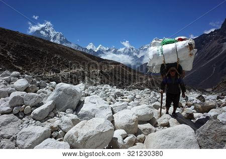 Sagarmatha national park, Nepal - May 20, 2019: Porter is carrying extremely big load hiking in riverbed. Everest trek, trail near Dughla (4620 m)