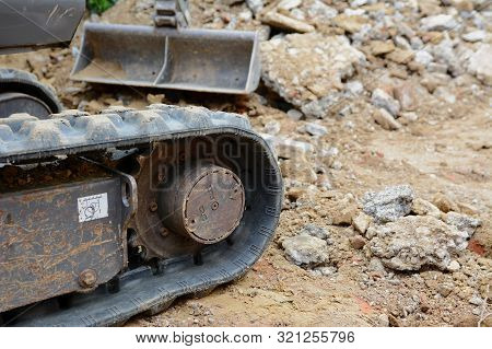 Rubber Track Of A Mini Digger In Selective Focus Against Background Of Concrete And Earth Excavation