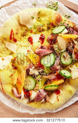 Pita with duck fillet and vegetables on craft paper and wood plate topview. Freshly baked yeast round flatbread with sliced goose fillet, melted cheese, cucumbers, tomatoes and spices