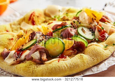 Pita with duck fillet and vegetables on craft paper and wood plate closeup. Macro shot of freshly baked yeast round flatbread with sliced goose fillet, melted cheese, cucumbers, tomatoes and spices