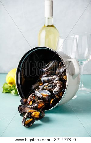 Pot of steamed mussels with lemon, herbs and white wine on blue background