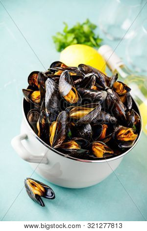 Pot of steamed mussels with lemon, herbs and white wine on blue background