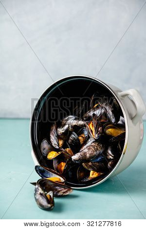 Pot of steamed mussels on blue background