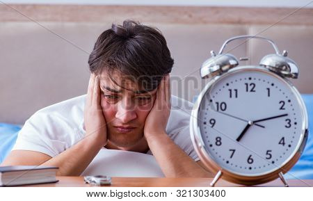 Man in bed frustrated suffering from insomnia with an alarm cloc
