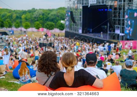 Friends watching concert at open air music festival, back view, stage and spectators at background