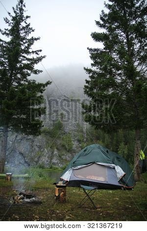 Tent On The Bank Of The River Amid Rocks In The Fog In The Early Morning