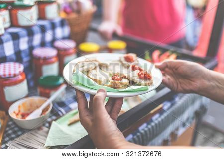 Close Up Of Hand Holding Plate With Bread Slices And Ajvar Samples At Street Market Food Festival.