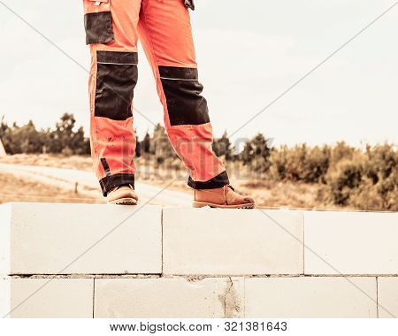 Low Section Legs Of Construction Worker Wearing Workwear Trousers And Brown Leather Work Boots Stand