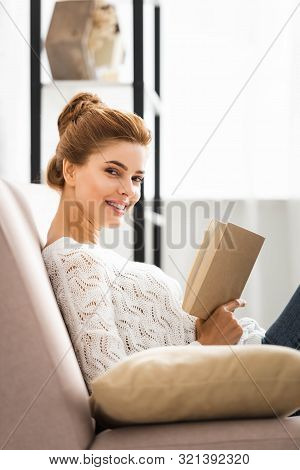 Attractive Woman In White Sweater Holding Book And Looking At Camera