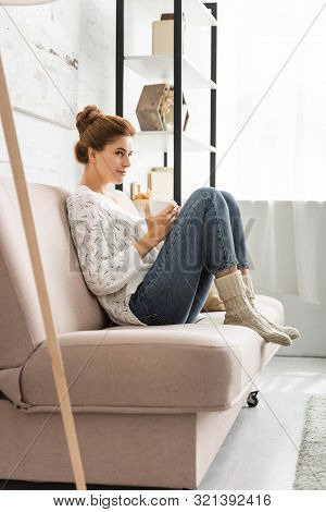 Attractive Woman In White Sweater Holding Cap And Looking Away