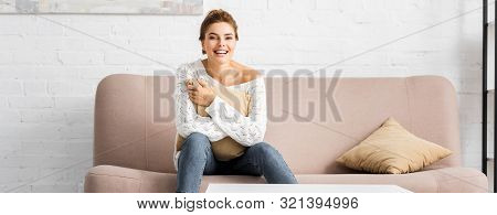 Panoramic Shot Of Attractive Woman In White Sweater Holding Pillow And Looking At Camera