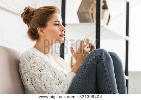 Attractive Woman In White Sweater Holding Cup And Looking Away