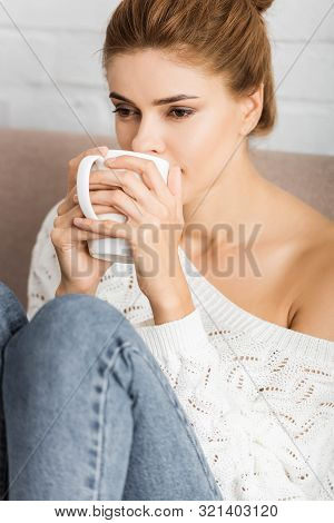 Attractive Woman In White Sweater Holding Cup And Looking Away
