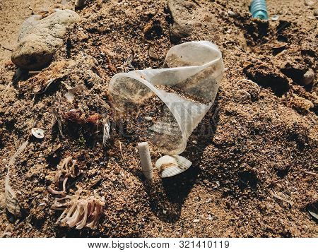Single Use Plastic Cup And Cigarette Butt In Sand, Marine Trash On The Beach. Plastic Pollution On T