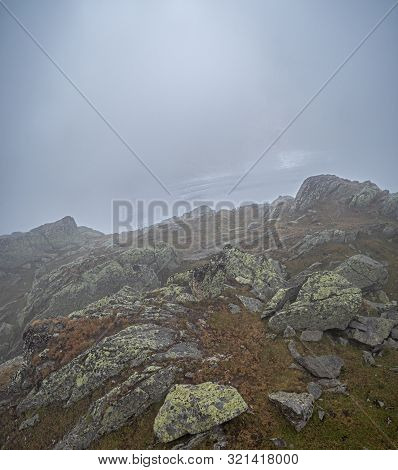 Clouds, Thick Fog And Mist Hide The View From The Alpine Rocks Toward A Galcier In The Background.  