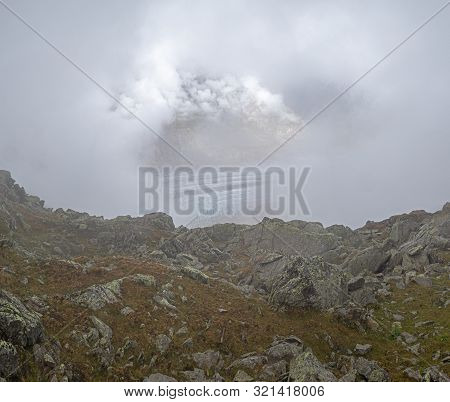 Clouds, Thick Fog And Mist Hide The View From The Alpine Rocks Toward A Galcier In The Background.  