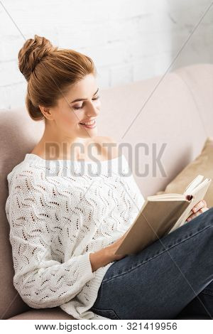 Attractive Woman In White Sweater Smiling And Reading Book