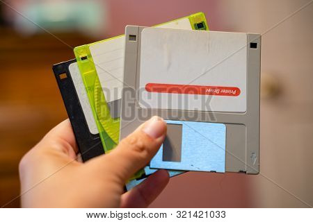 Hand Holds Out Three Outdated 3.5 Inch Floppy Disks, From The 1990s